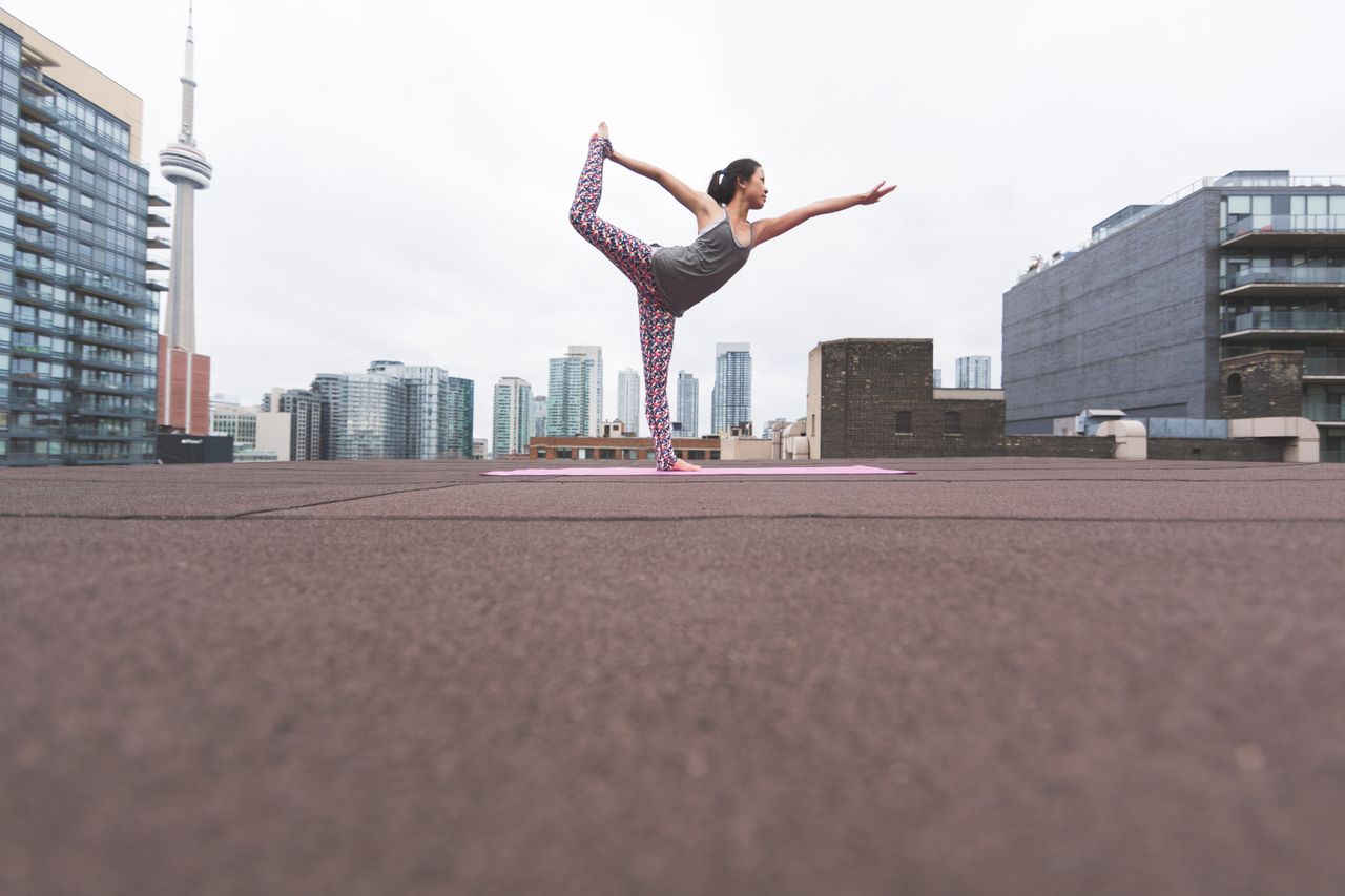 Woman practicing yoga on a rooftop with Toronto skyline in the background.