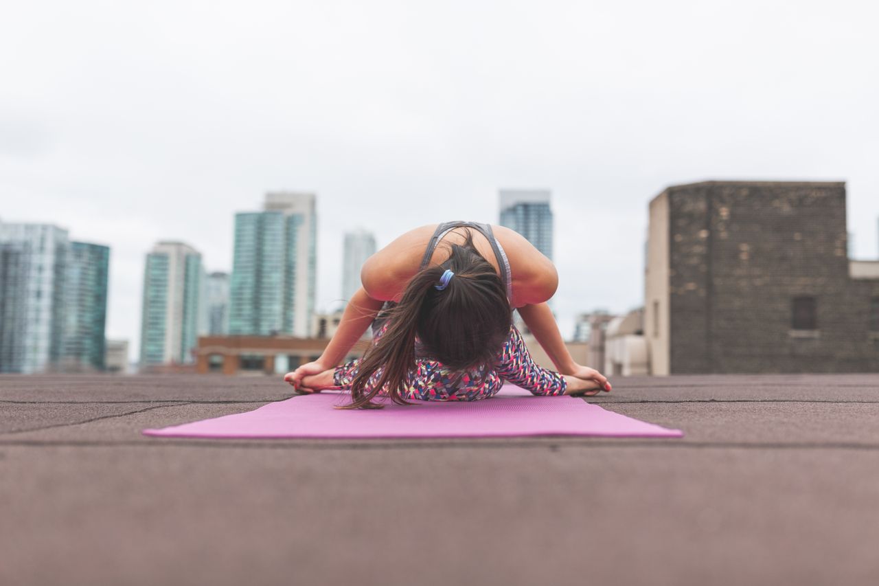 Young woman performing yoga poses on a rooftop with urban skyscrapers in the background.