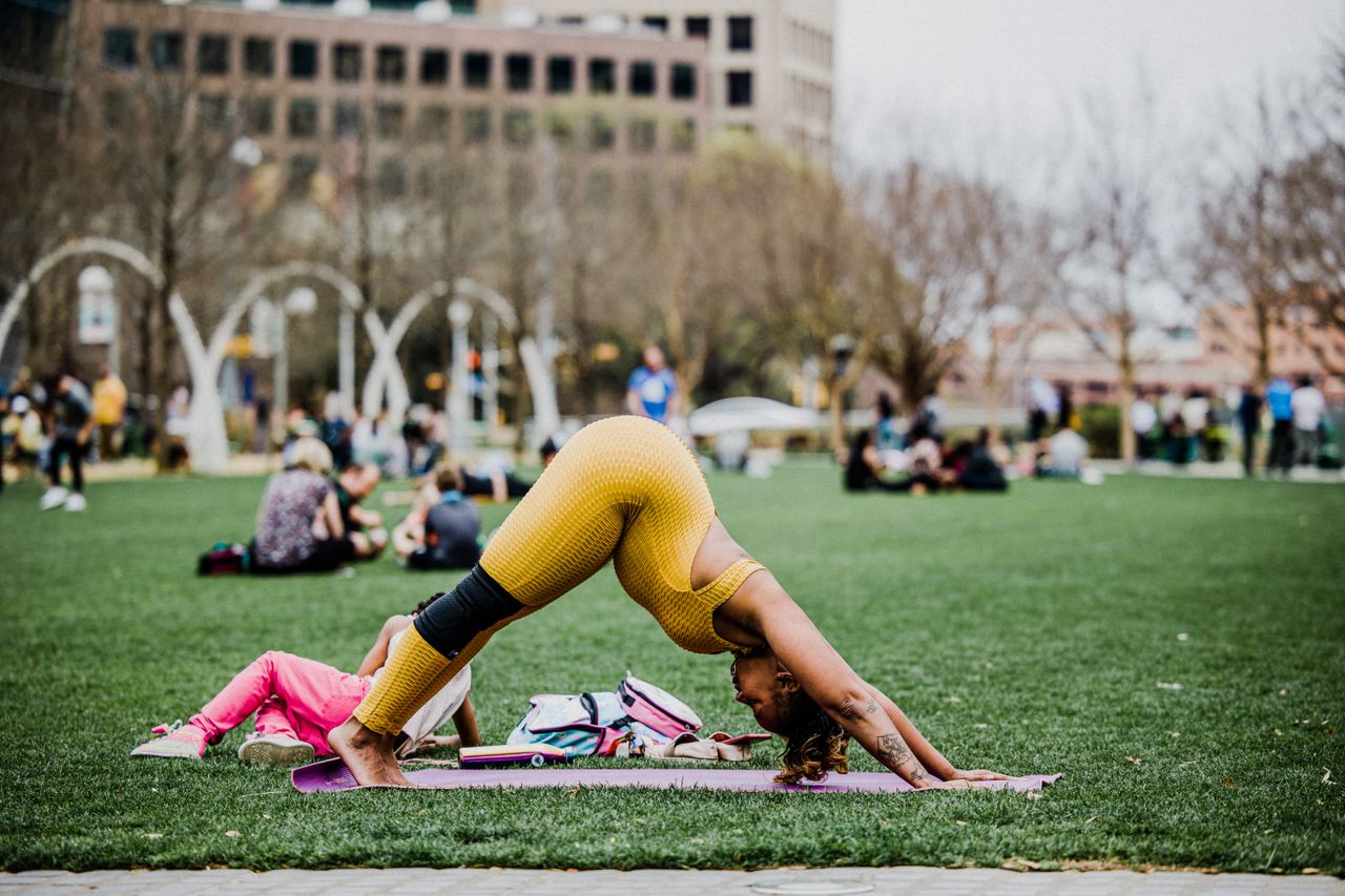 Side view full body of pregnant African American female practicing Downward Facing Dog with Toe Raises on sports mat in city park