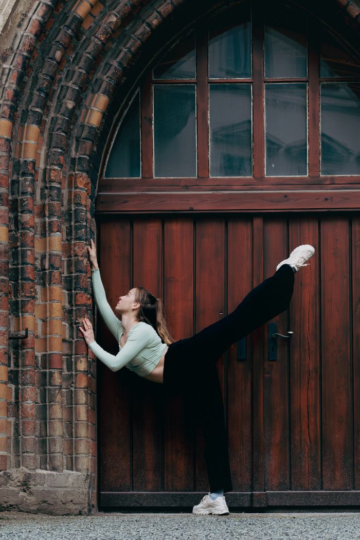 Woman in black pants and green crop top stretching against a historic archway.